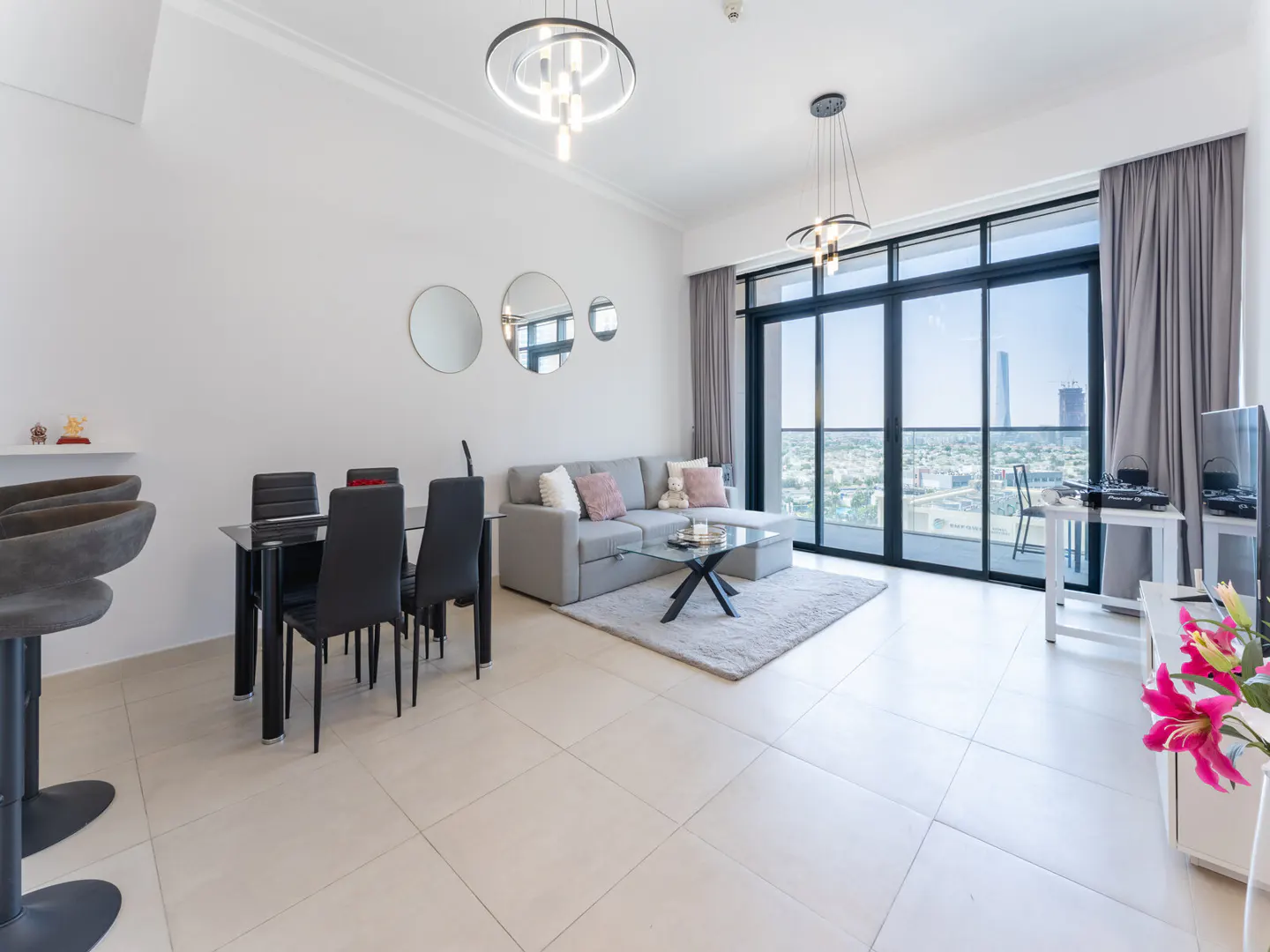 Bright, modern apartment interior with a gray sofa, black dining set, and city view from a large balcony.