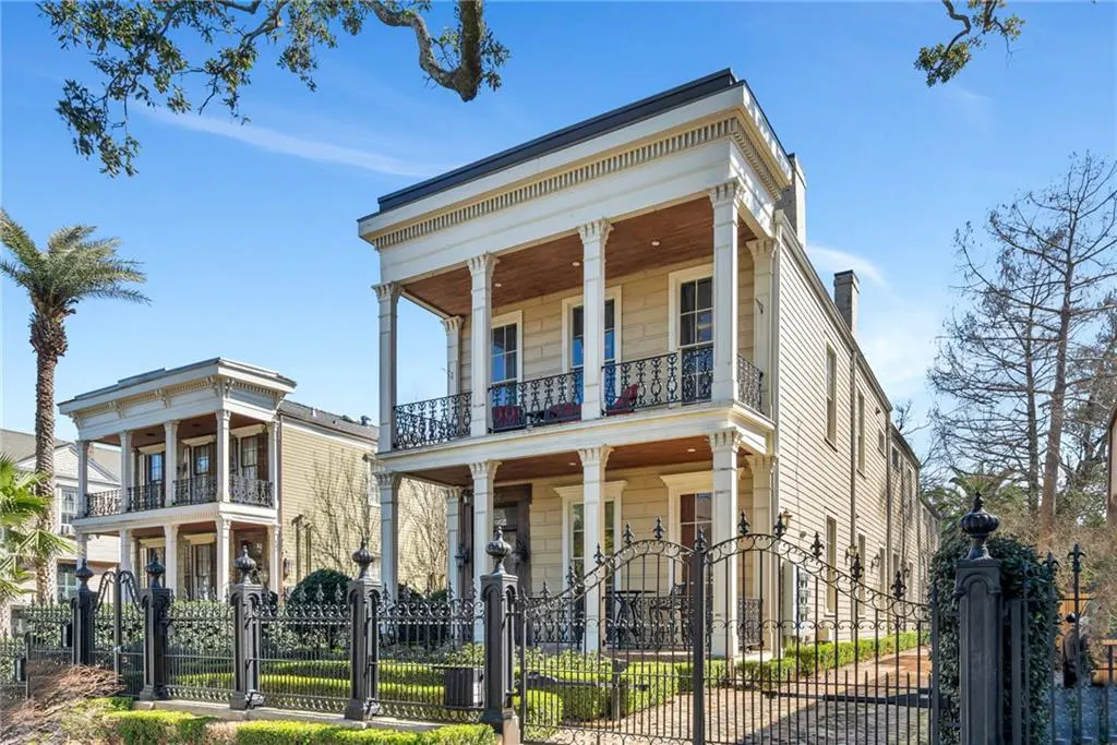 Two-story historic home with cream siding, white columns, and double-level balconies behind a black iron fence.
