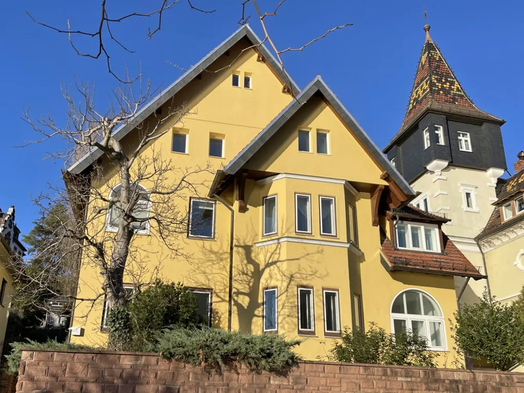 Exterior view of a yellow two-story house with a tower, set against a clear blue sky.