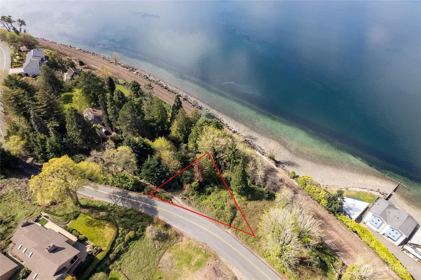 Aerial view of a vacant lot outlined in red, nestled between a road and the Puget Sound shoreline with trees.