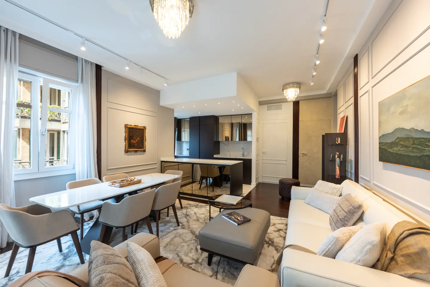 Modern open-plan living room with a white dining table, cream chairs, white sofa, and a sleek dark kitchen in the background.