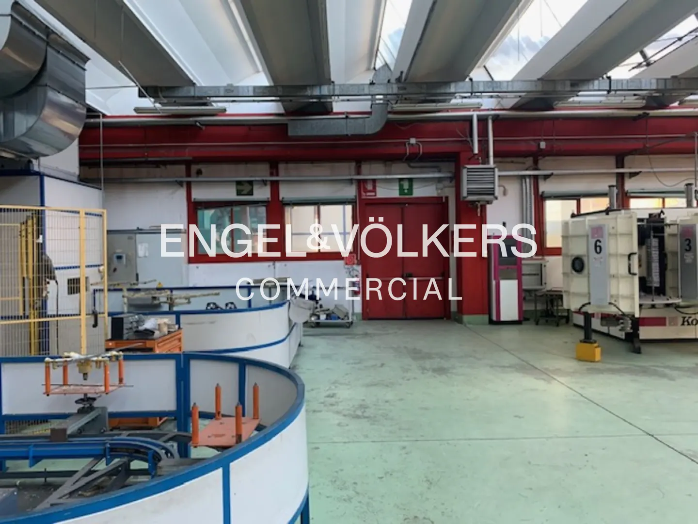 A commercial space with machinery, a conveyor belt, and red doors in the background. The floor is light green.