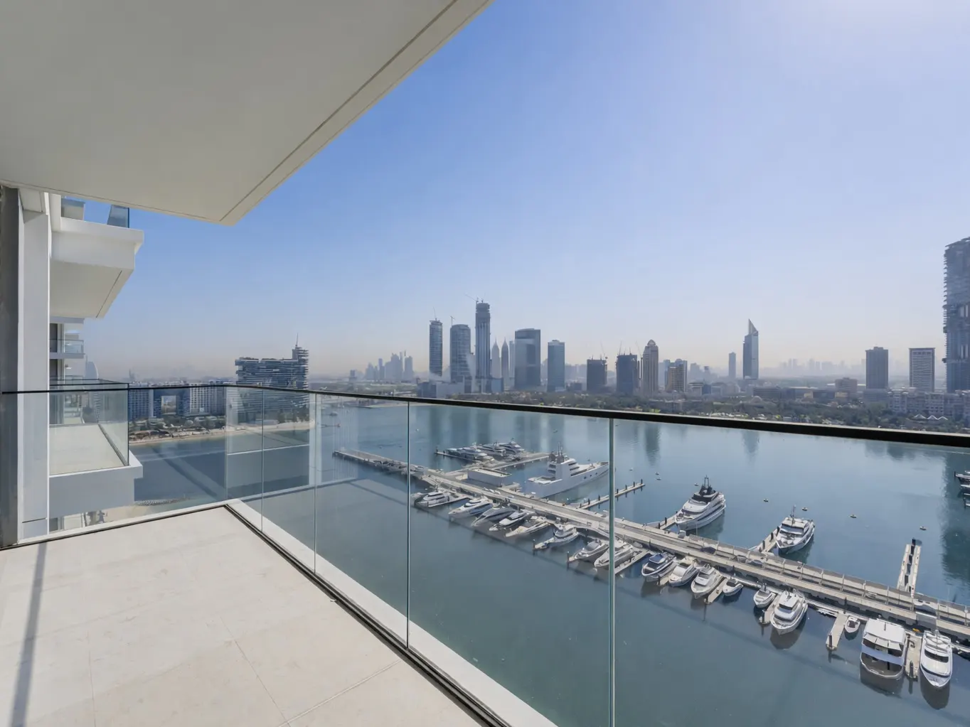 Balcony view of Dubai skyline, yachts in harbor. Glass railing, white floor. Blue sky.