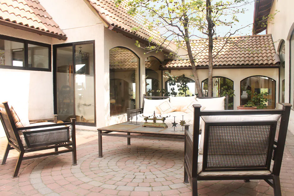 Outdoor patio with brick flooring, seating, and a table. The building has a tile roof and arched windows.