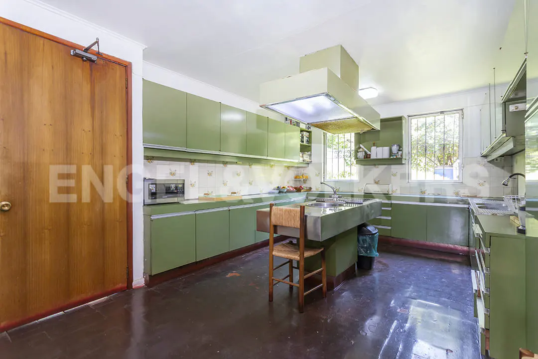 A kitchen with green cabinets, a center island with a sink, and a wooden chair. A window is visible in the background.