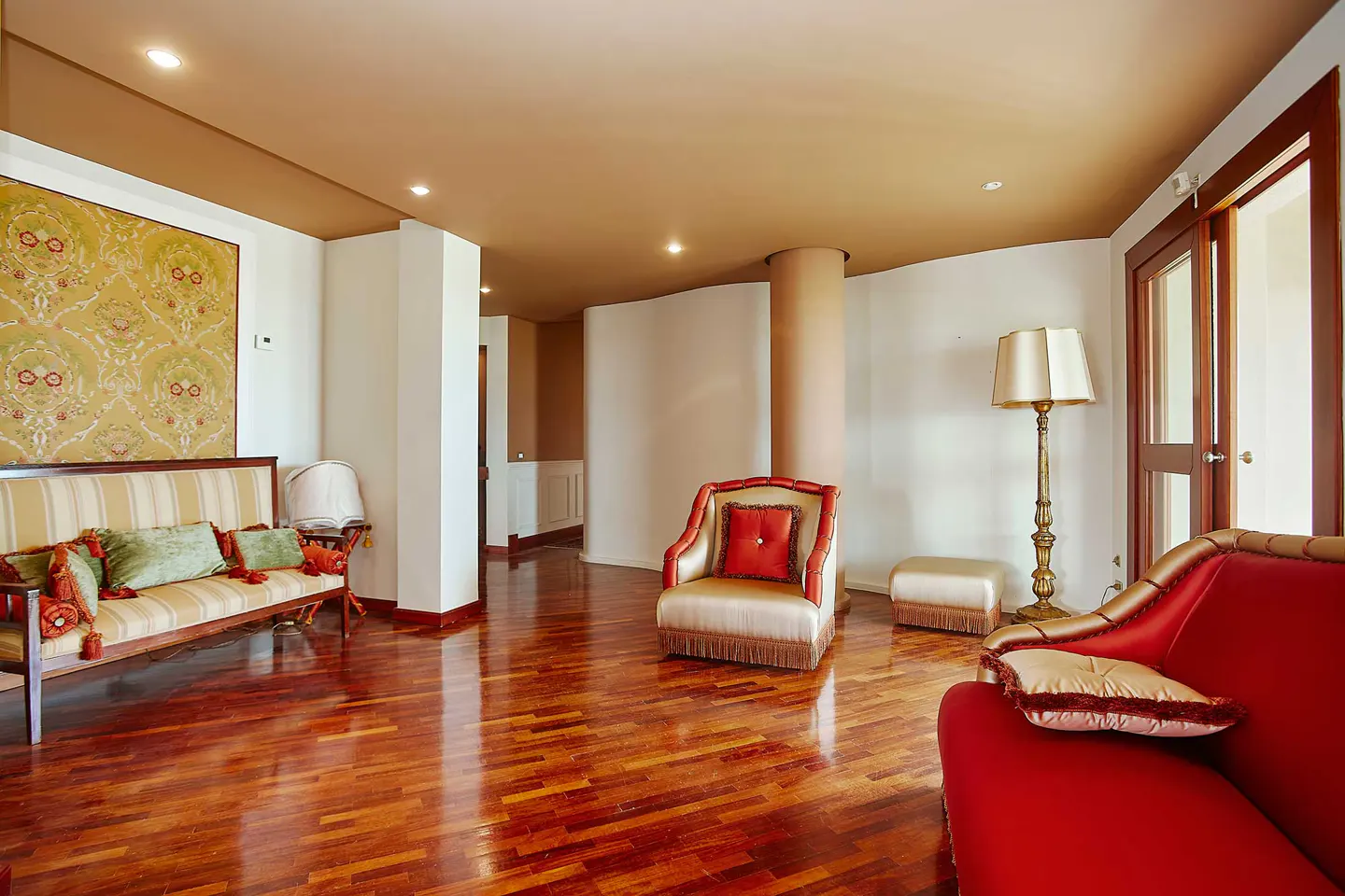 A living room with a red sofa, a beige armchair, and a striped couch with green pillows on a shiny wooden floor.