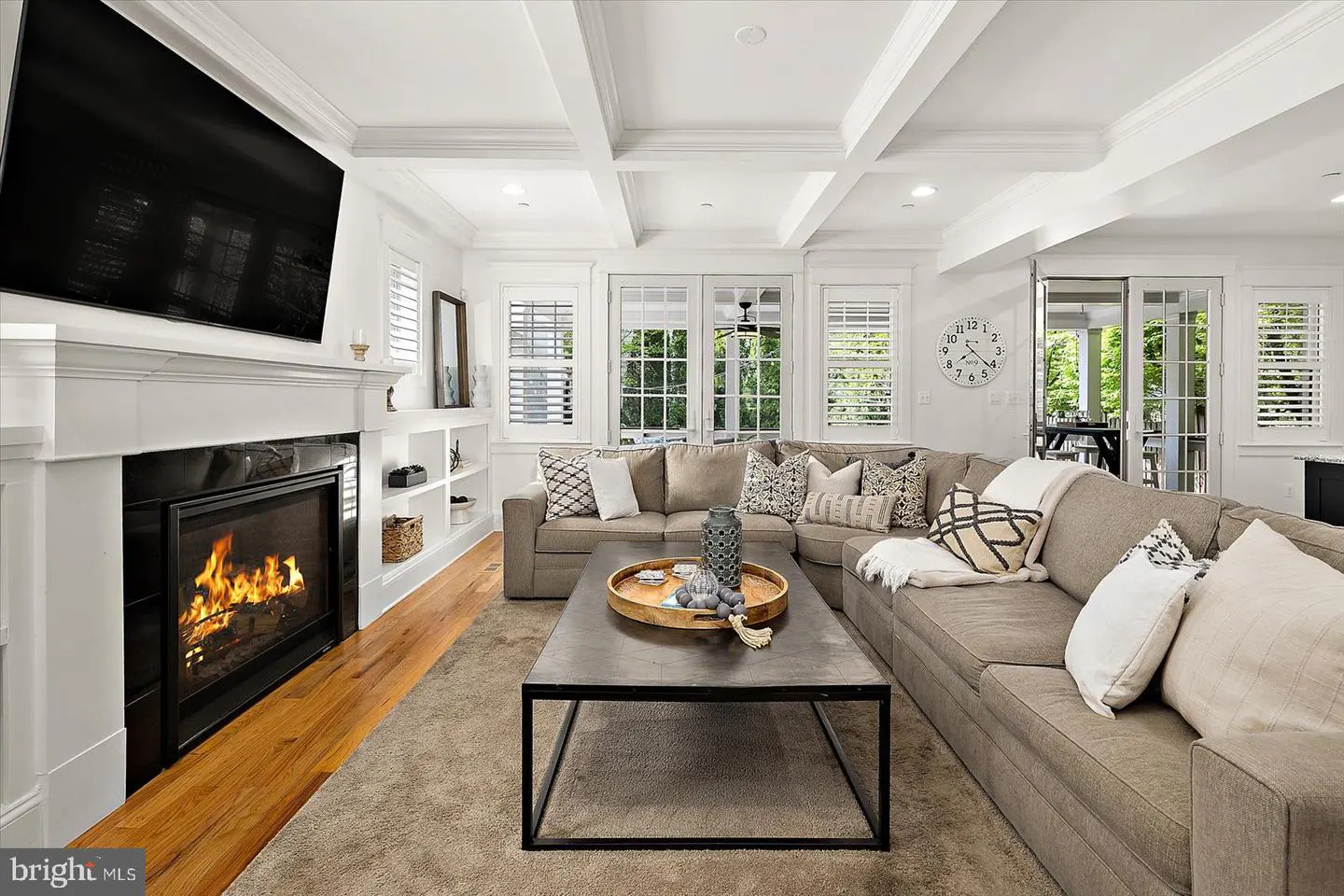 Bright living room with a large gray sectional sofa, a black metal coffee table, and a fireplace with a TV above it.