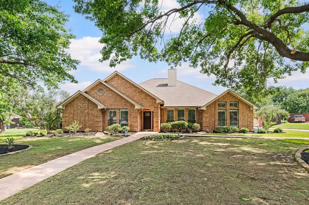 A single-story brick house with a brown roof, green lawn, and trees.