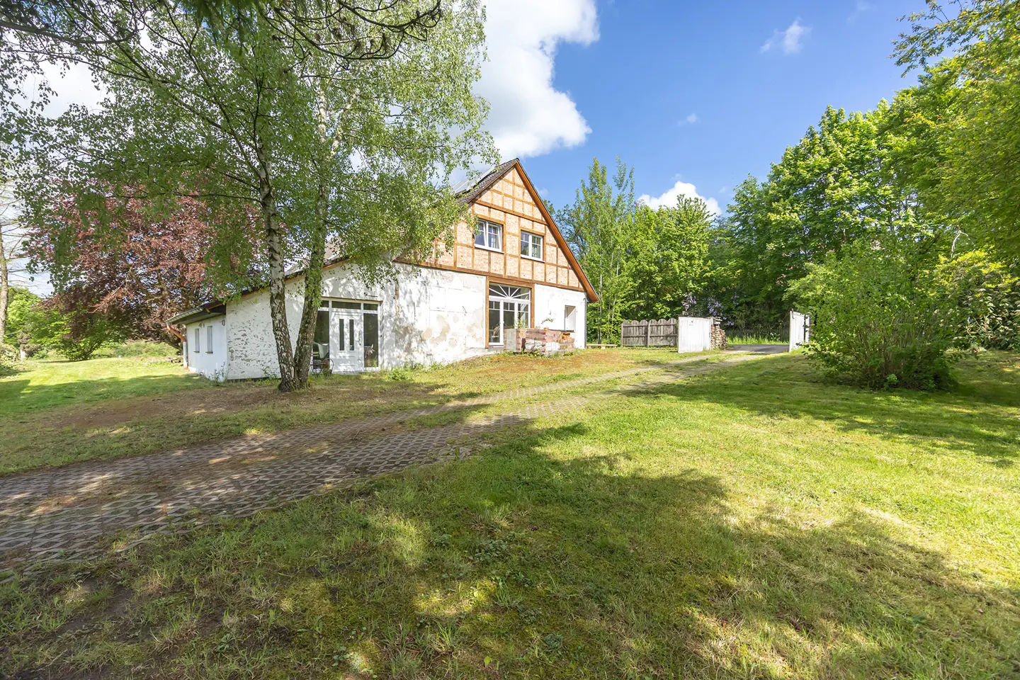 Exterior of a white, two-story house with a brown, half-timbered gable roof, surrounded by green grass and trees.