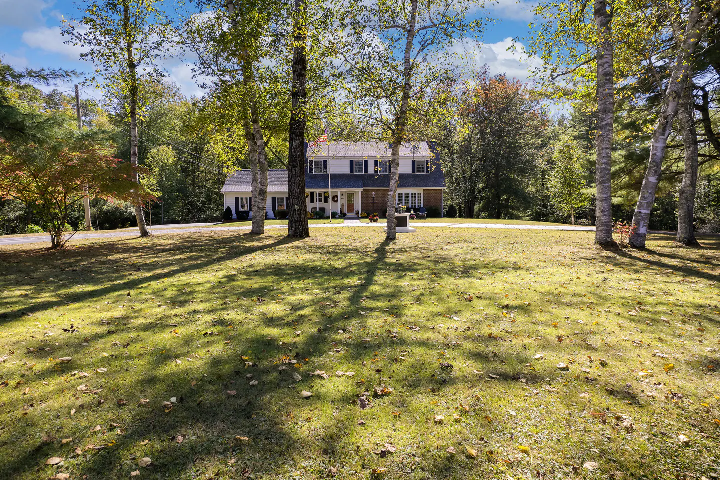 Two-story house with gray siding and white trim, viewed across a large lawn with trees.