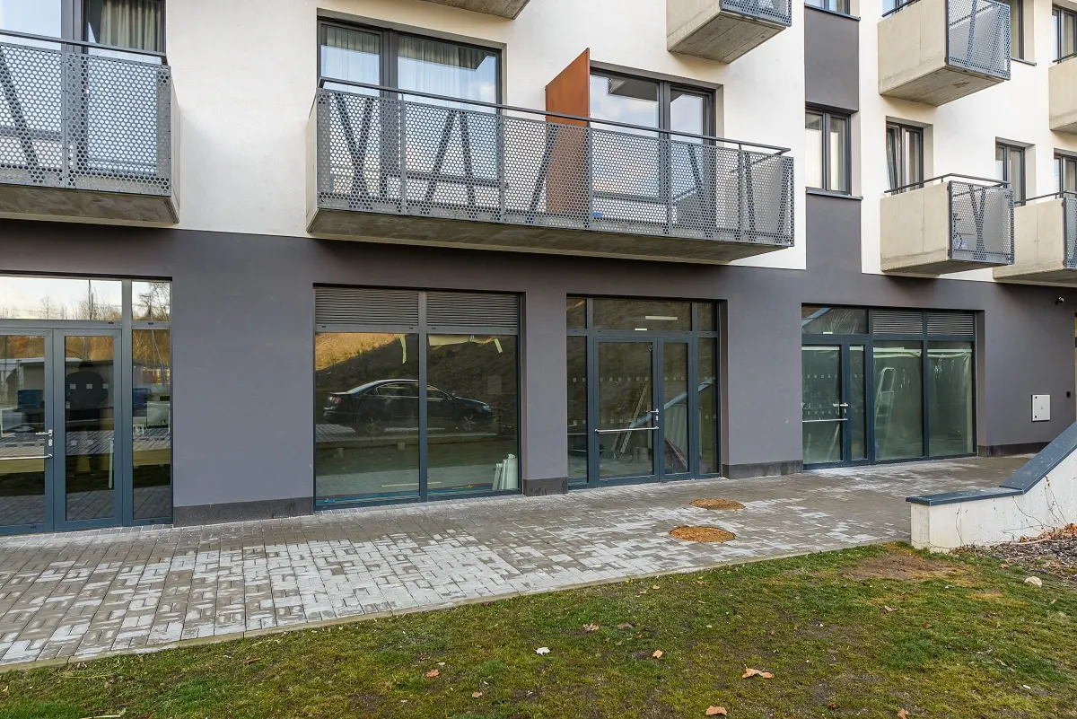 Modern apartment building exterior with gray ground-floor storefronts, glass doors, and metal balconies above.