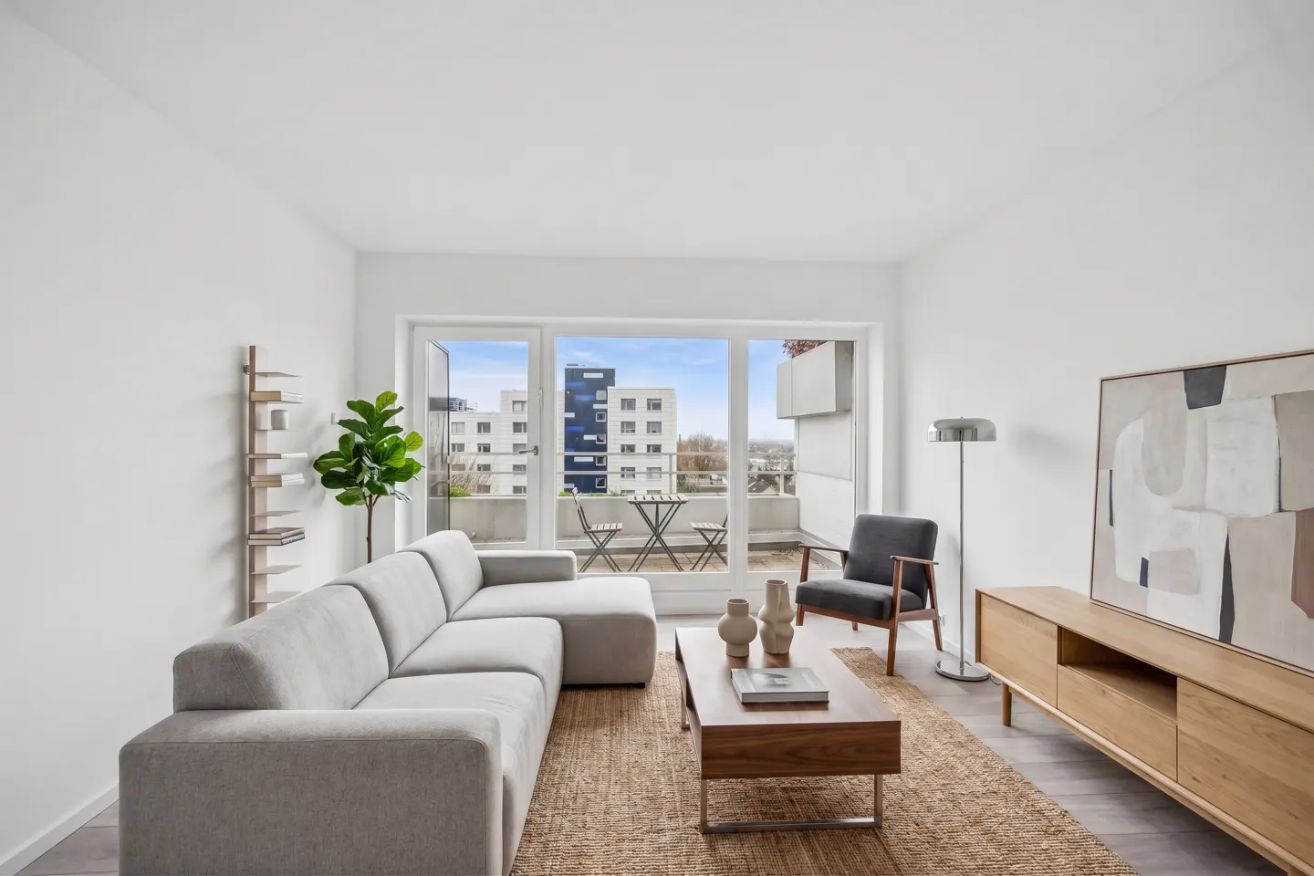 Bright living room with a gray sectional sofa, wood furniture, and a balcony with a city view.