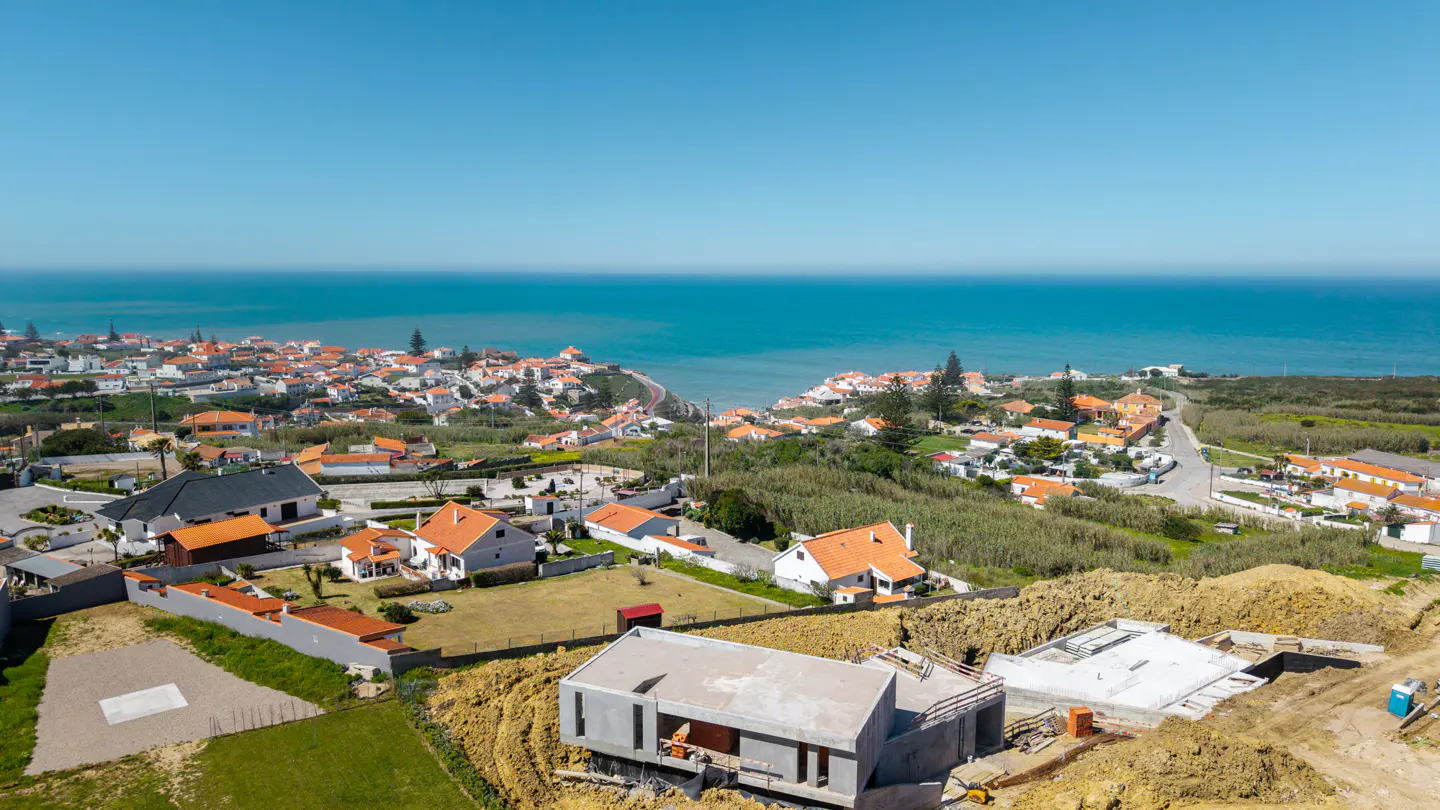 Aerial view of a modern home under construction, with ocean and town in the background on a sunny day.