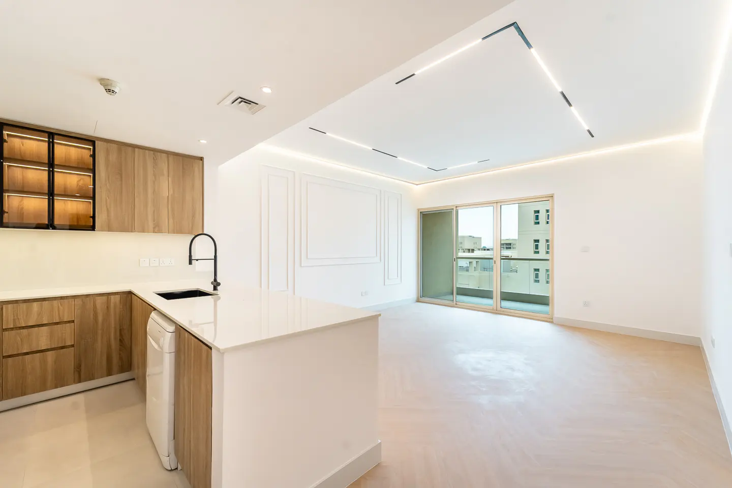 Bright, modern kitchen with wood cabinets, white countertops, and a black faucet. A sliding glass door leads to a balcony.