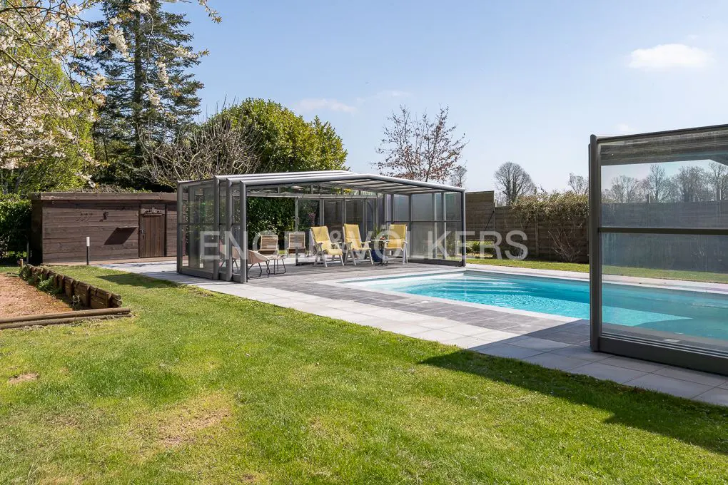 Outdoor pool with a retractable enclosure, surrounded by green lawn and trees under a blue sky.