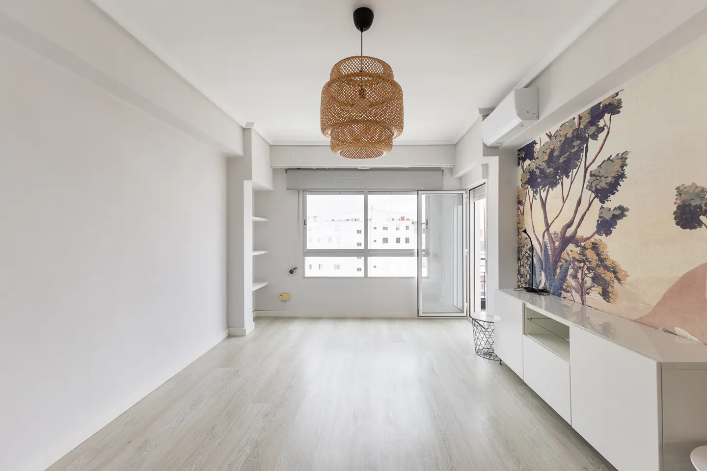 Bright room with light wood floors, a woven pendant light, and a wall featuring a large, colorful tree mural.