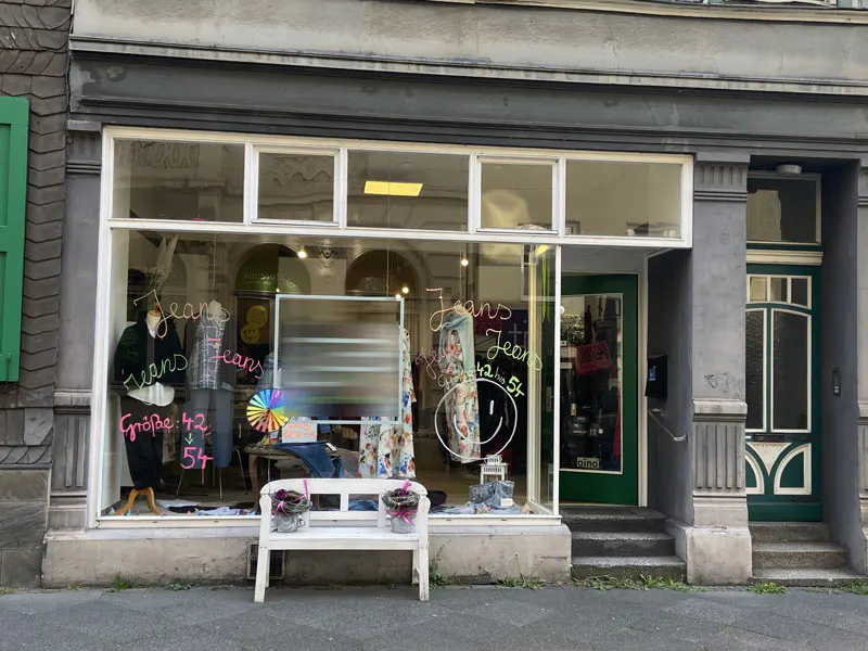 Street view of a jeans shop with a white bench in front of the window. Mannequins and clothes are visible inside.