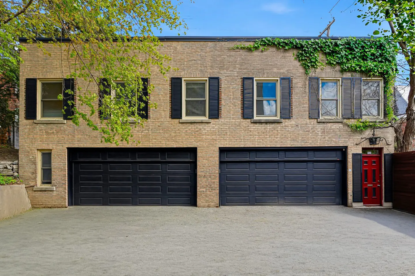 Two-story brick building with two black garage doors, black shutters, and a red front door. Green ivy climbs the right side.