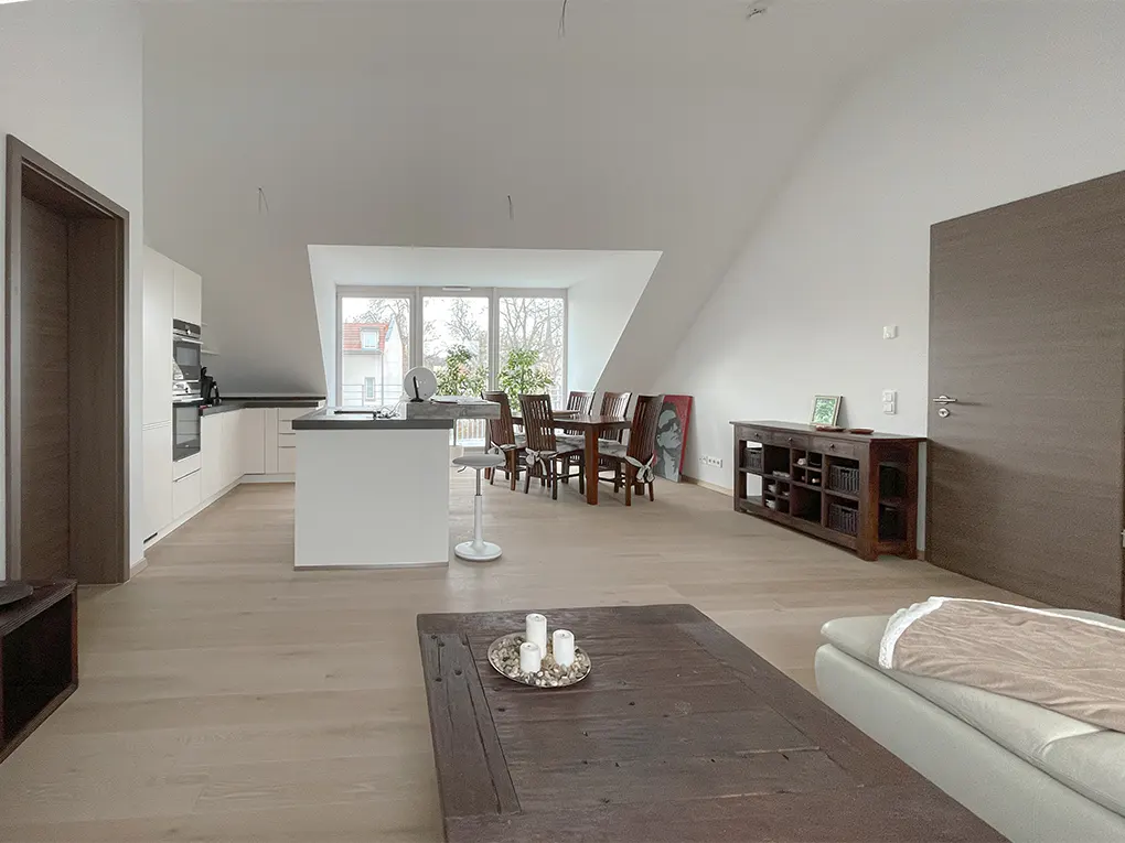 Bright, open-plan living space with white walls, light wood floors, kitchen, dining table, and dark wood coffee table.