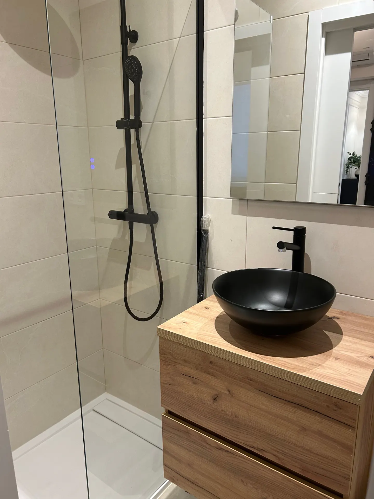 Bathroom with a black shower, glass door, and a wood vanity with a black sink and faucet. A mirror hangs above the sink.
