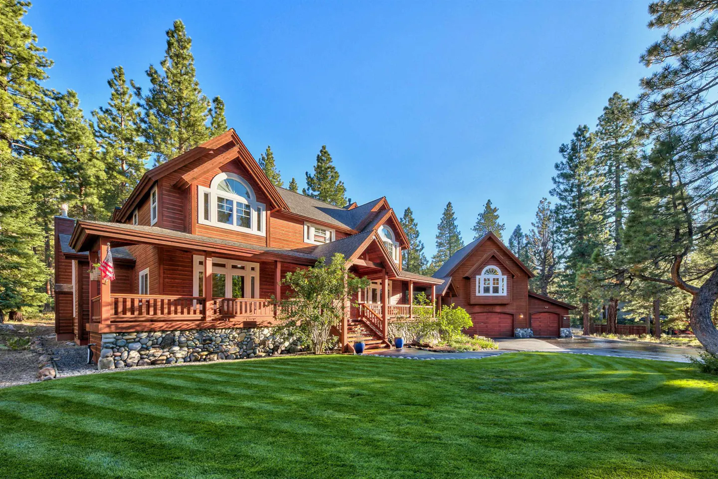 A two-story wood house with a porch and a large lawn surrounded by trees.