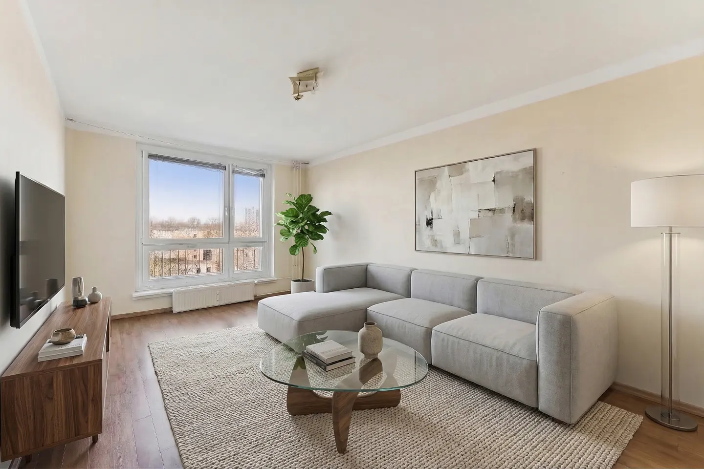 Living room with a gray sectional sofa, glass coffee table, TV, and a large window with a city view.