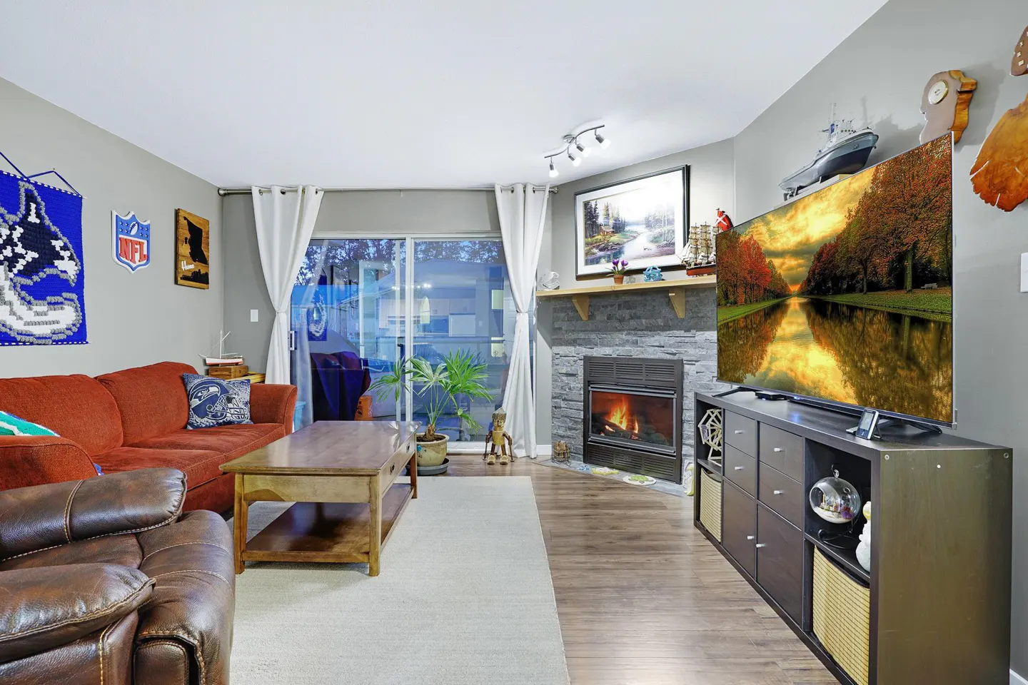 Living room with a red sofa, brown leather chair, fireplace, and a TV showing a fall landscape.