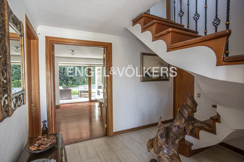 Entryway with wooden staircase, decorative driftwood sculpture, and a view through a doorway to a patio and garden.
