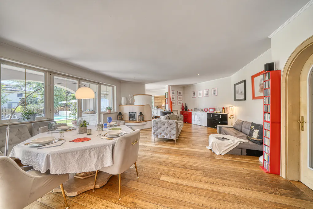 Open-concept living space with wood floors, a dining table set for a meal, and a gray sofa. Large windows offer natural light.