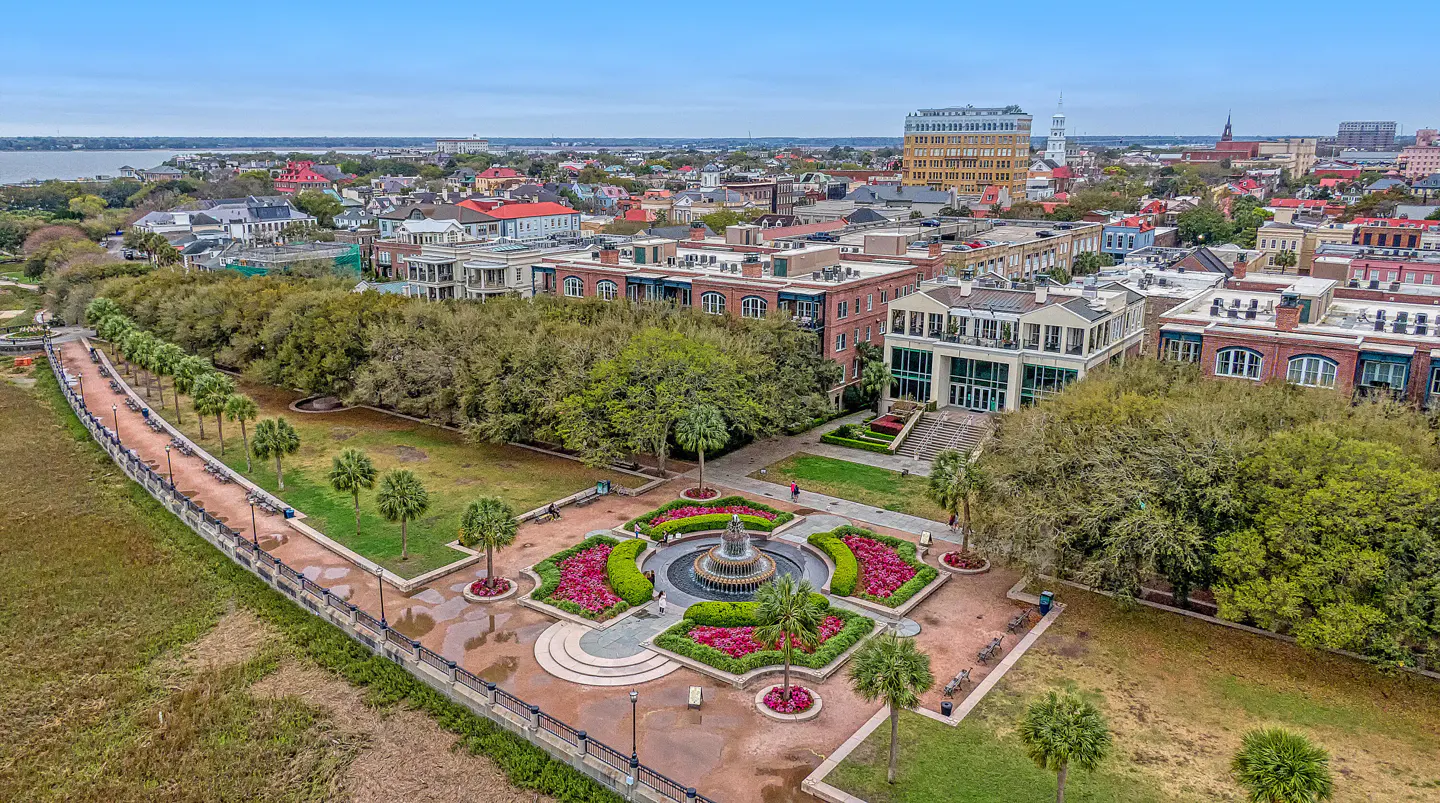 Aerial view of Charleston's Waterfront Park, featuring a fountain, walkway, and city skyline in the background.