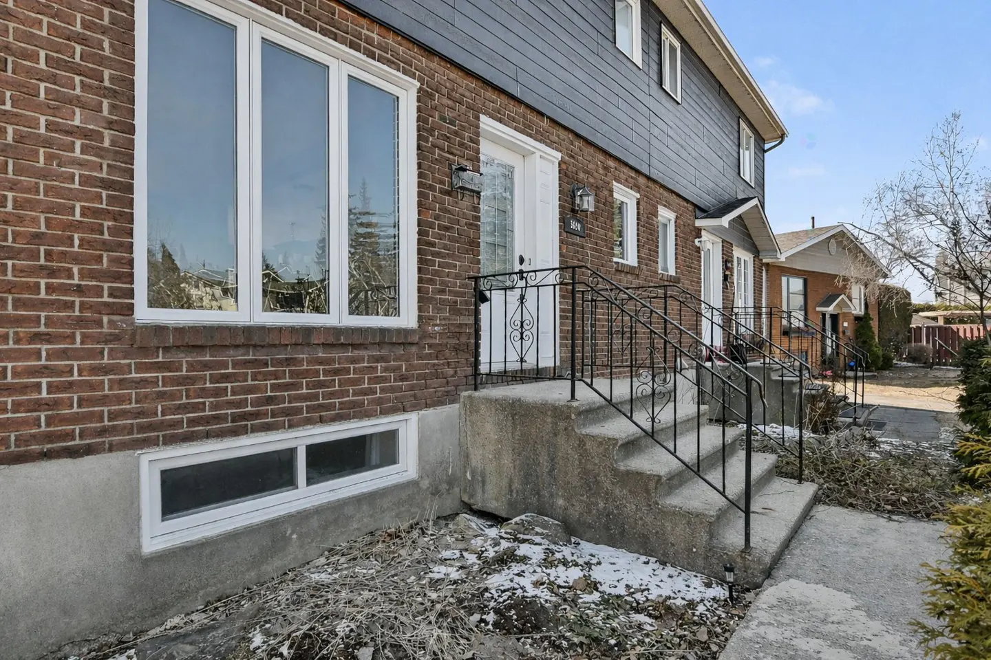 Exterior view of a brick townhouse with a white door and black railing leading to the entrance.