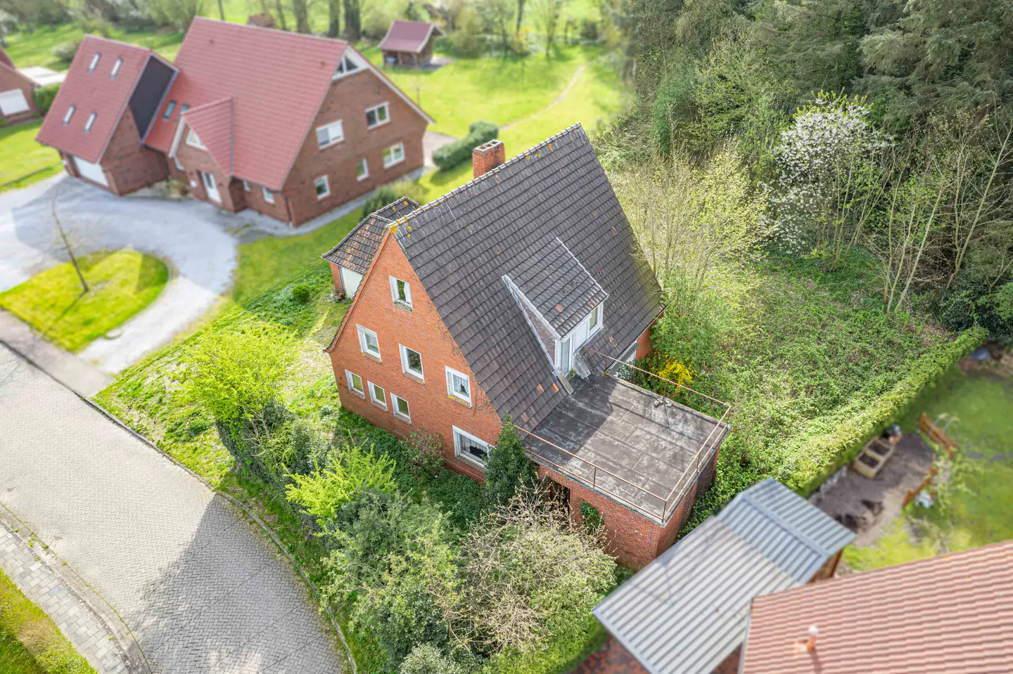 Aerial view of a red brick house with a gray tiled roof, surrounded by green trees and lawns.