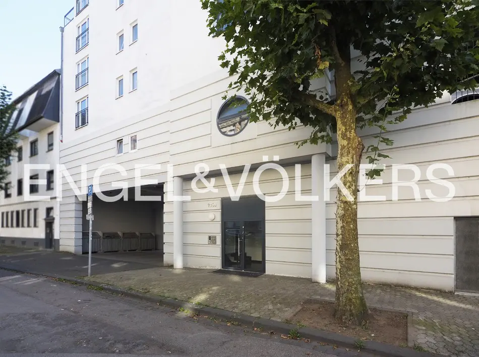 Modern white apartment building exterior with a ground-level entrance, circular window, and adjacent parking area.