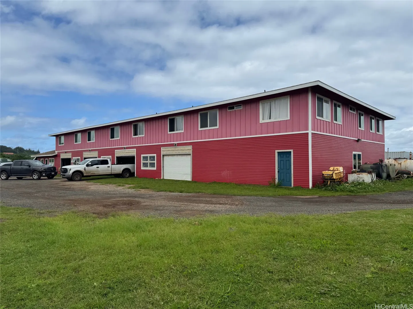 Two-story red building with white garage doors and windows under a cloudy sky. Two pickup trucks are parked in front.