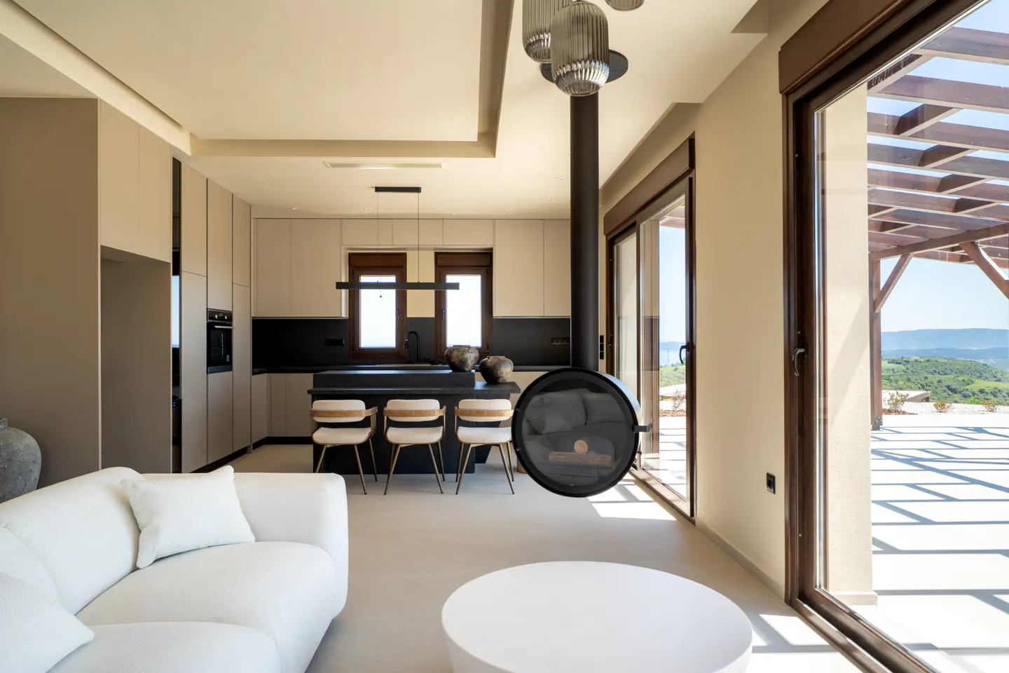 A modern, open-concept living space with a kitchen island, white sofa, and a hanging fireplace. Sliding glass doors lead to an outdoor patio.
