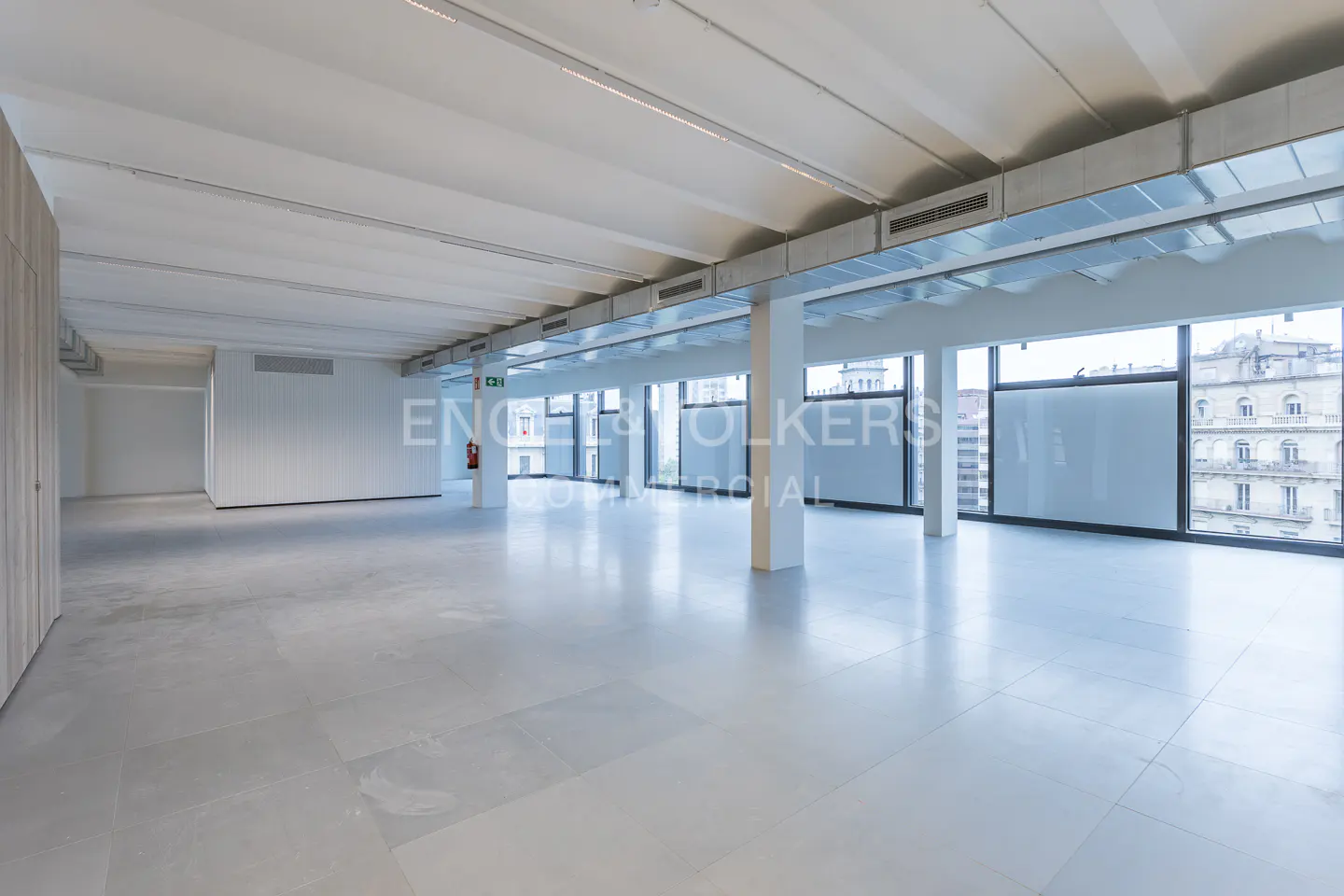 Bright, empty commercial space with white walls, gray floors, and large windows overlooking a city.