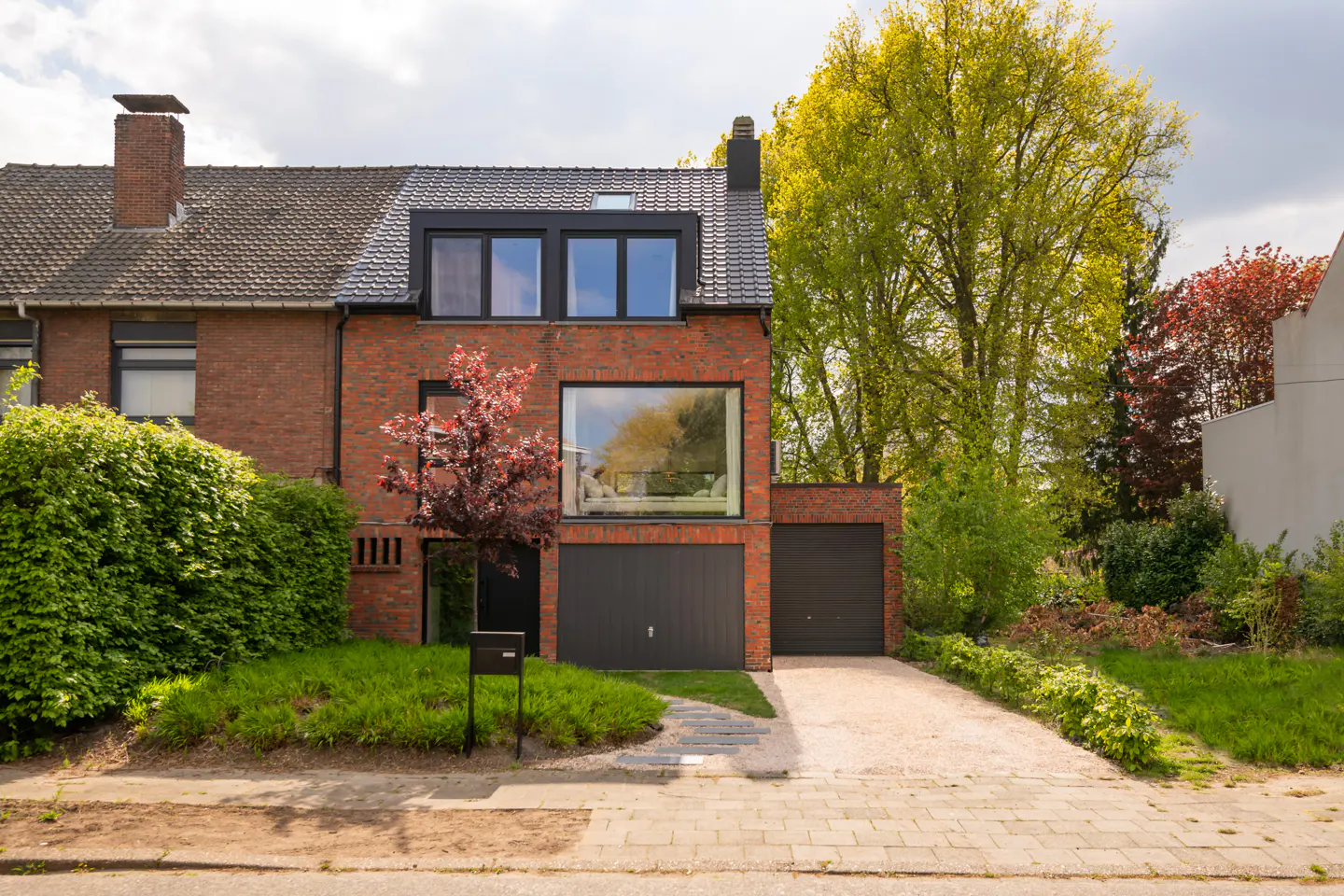 Brick house with two-car garage, black doors, and large window. Green trees and lawn surround the property.