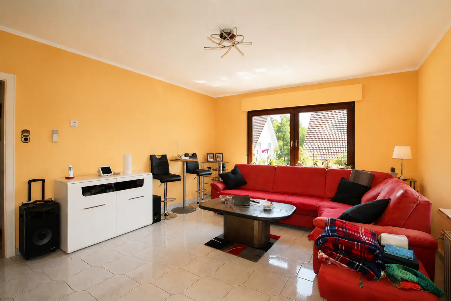 Living room with orange walls, a red sectional sofa, a coffee table, and a white cabinet on a light tiled floor.