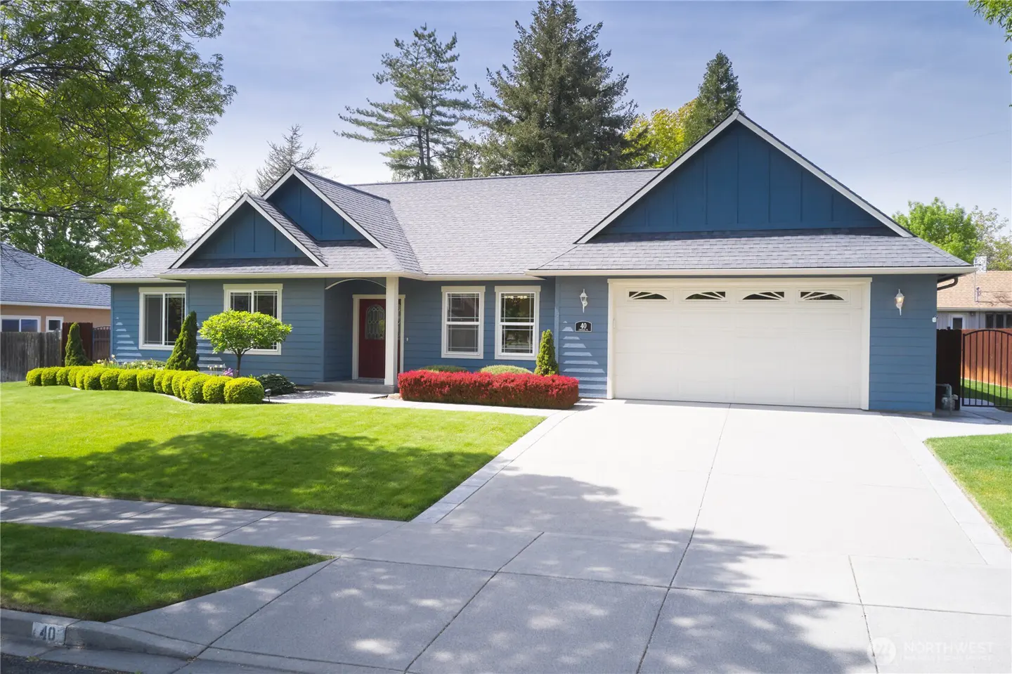 A blue single-story house with a gray roof, white garage door, red front door, and green lawn.