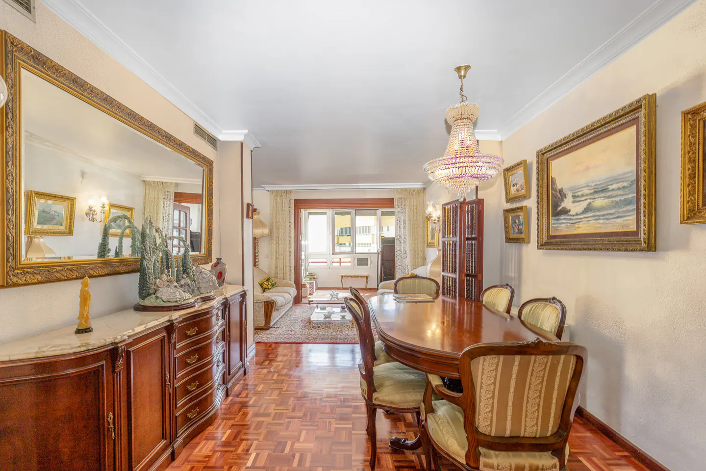 A formal dining room with a wood table, striped chairs, and a crystal chandelier. A large mirror and paintings adorn the walls.