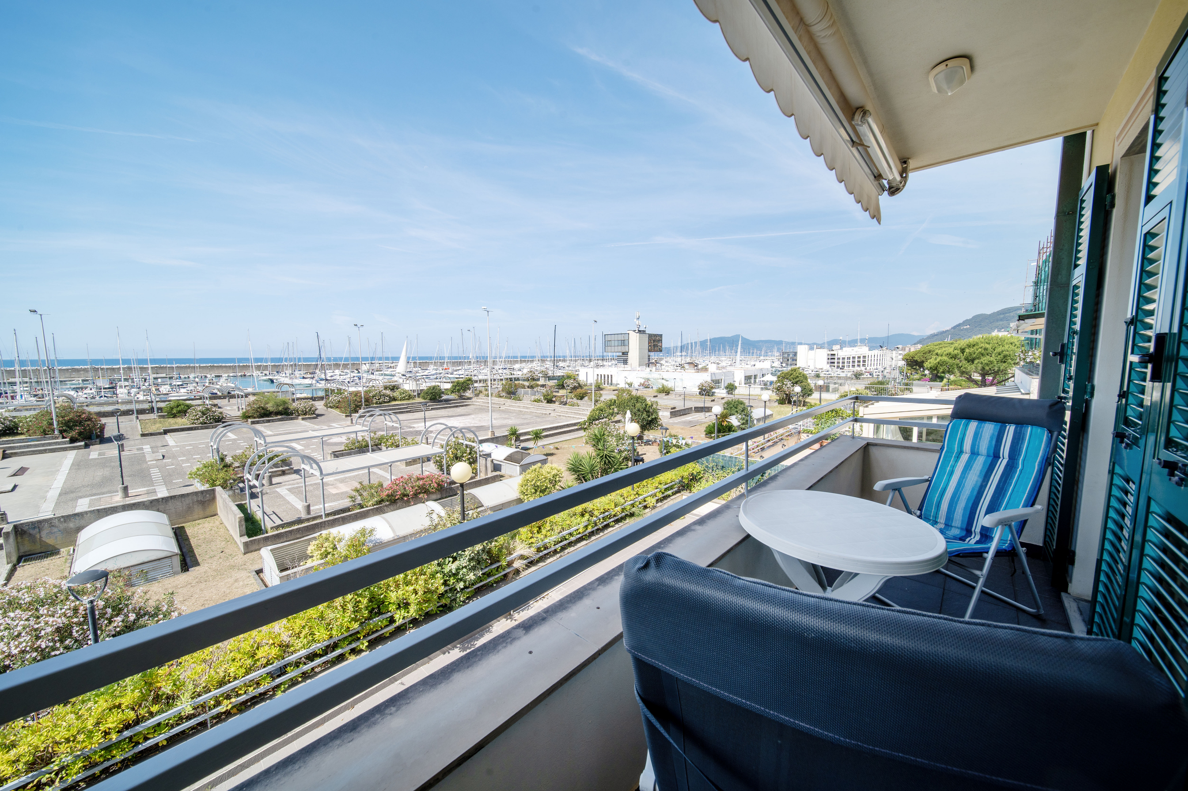 Balcony with a small table and chairs overlooking a sunny marina filled with sailboats under a clear blue sky.