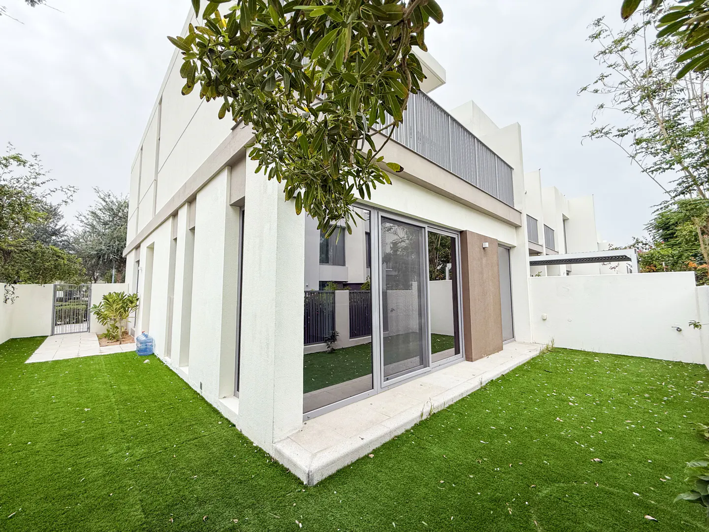 Exterior view of a modern, two-story white house with a green lawn and sliding glass doors.