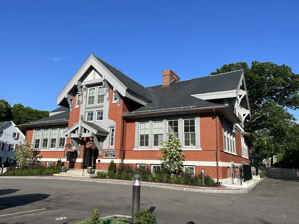 Exterior view of a two-story red brick building with gray trim and a black roof, set against a blue sky.