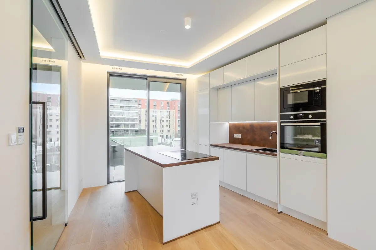 Bright, modern kitchen with white cabinets, wood floors, and a center island. A sliding glass door leads to a balcony with a city view.
