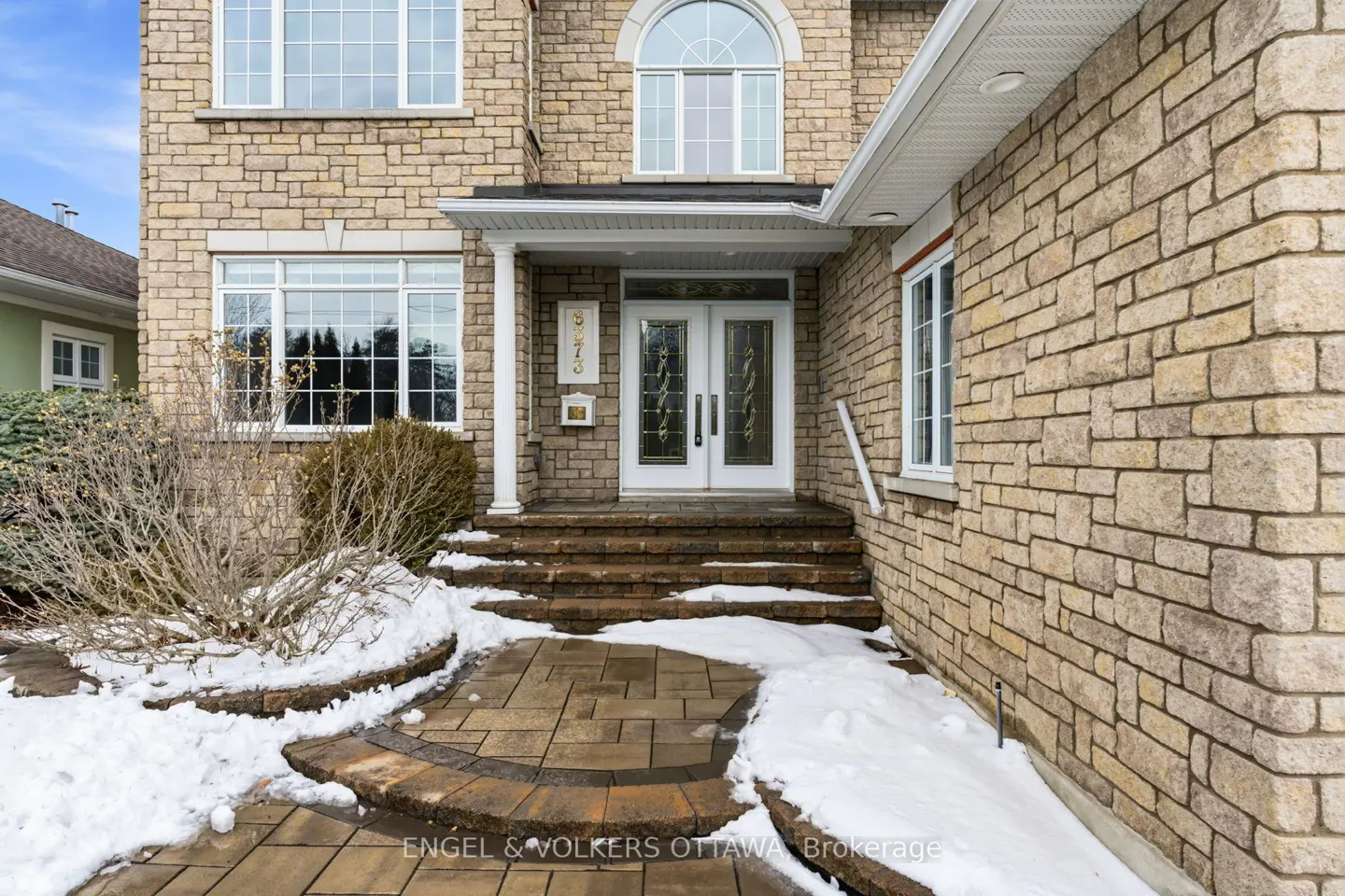 Exterior of a tan stone house with white trim, double doors, and snow on the ground.