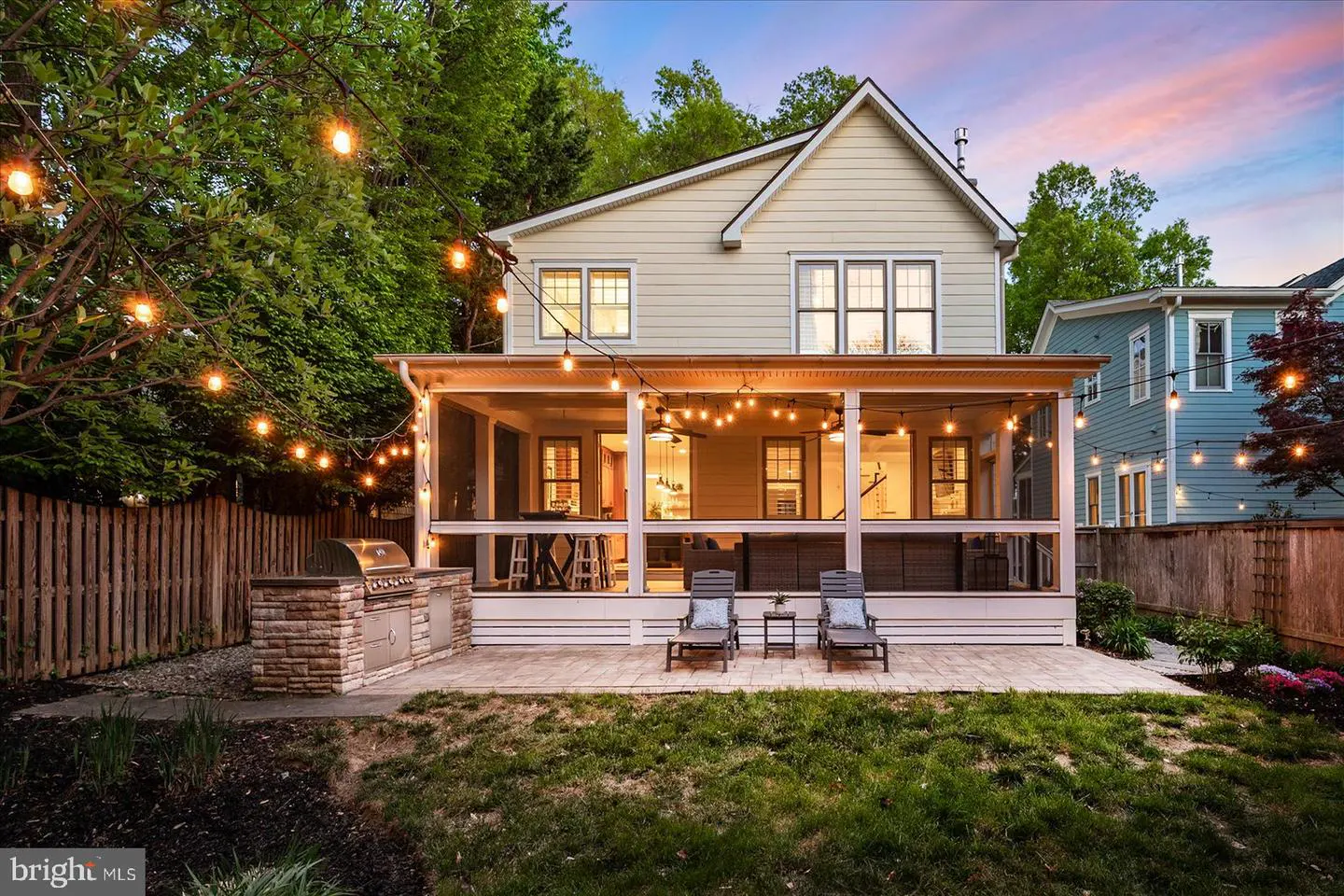 Backyard of a two-story house with a screened porch, grill, patio, and string lights.
