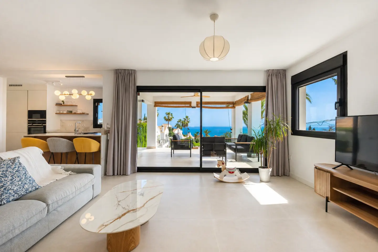 Modern living room with grey sofa, marble coffee table, and sliding doors opening to a terrace with sea views.