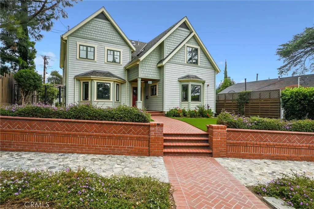 Two-story home with light green siding, dark green trim, and a red brick walkway leading to the front door. Brick retaining wall with flowers.