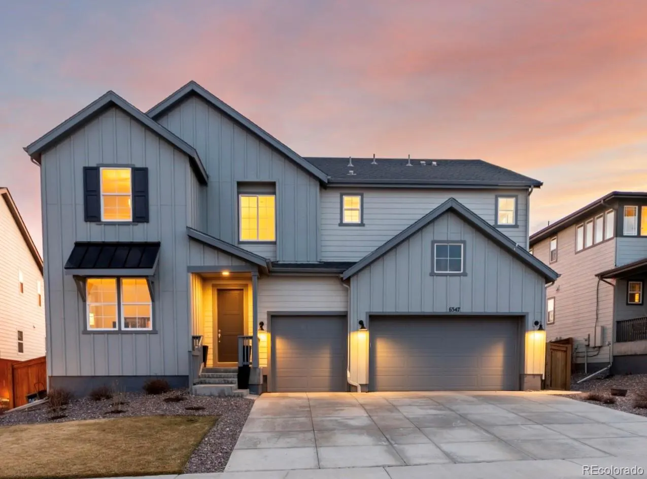Two-story gray house with a two-car garage and a concrete driveway at sunset.