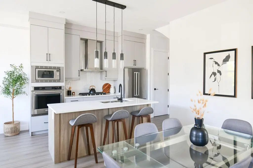 A modern kitchen and dining area with gray cabinets, a white countertop island with stools, and a glass dining table.